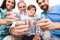 Family in sun-lit kitchen drinking water